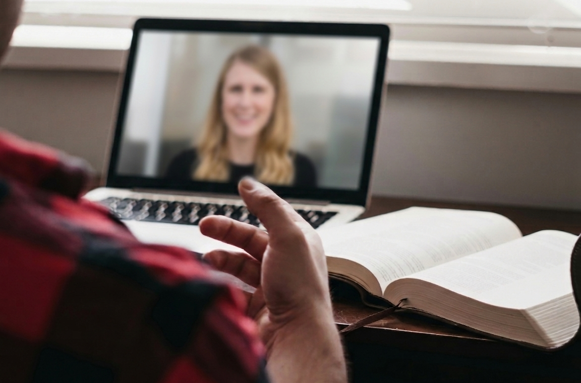 Person on a video call with a woman on a laptop, with an open book beside them.